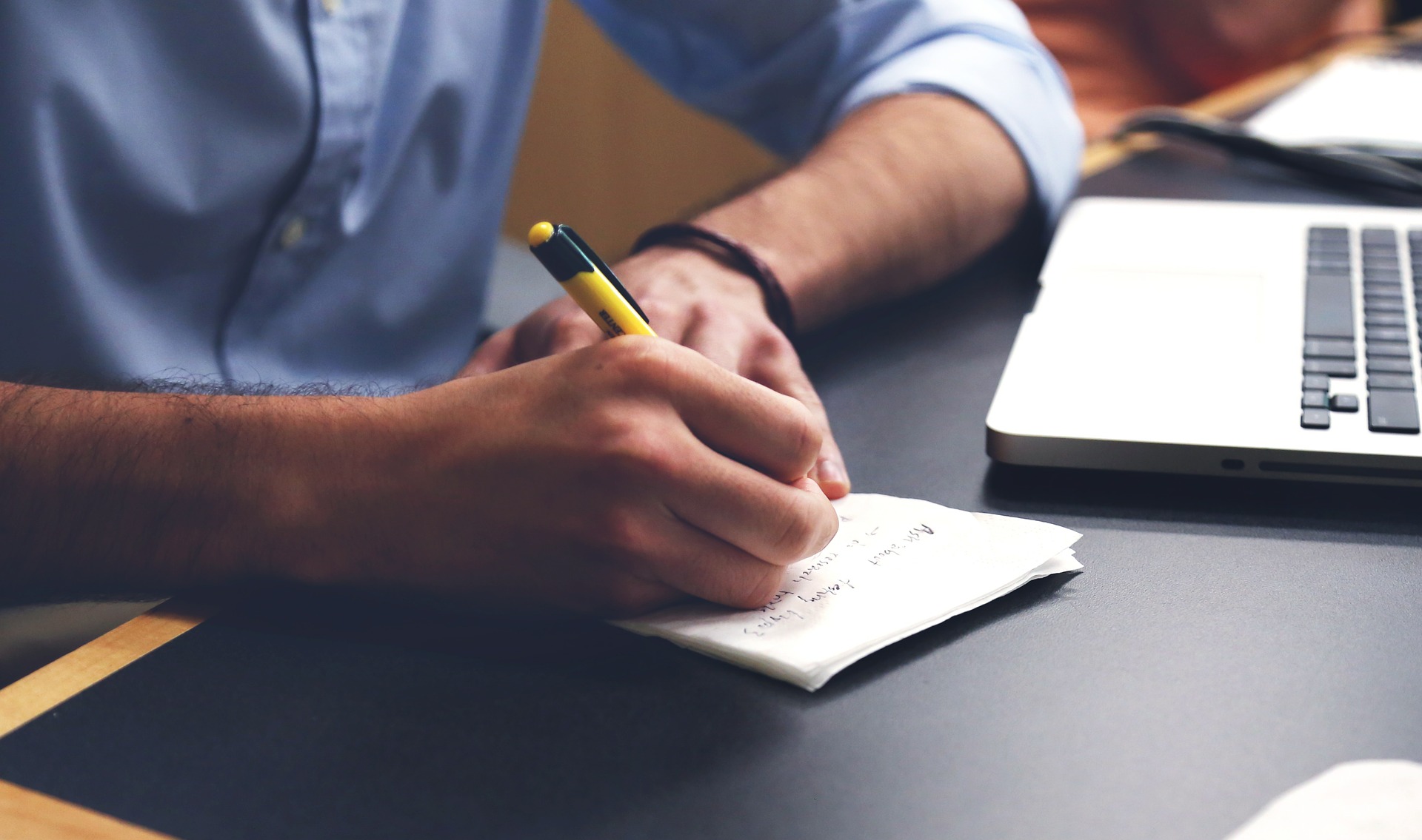 man writes on a pad as he looks at his laptop